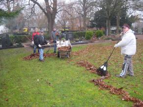 Die Volontäre entfernen Laub auf dem Friedhof