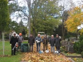 Volontäre beseitigen Laub auf dem Friedhof